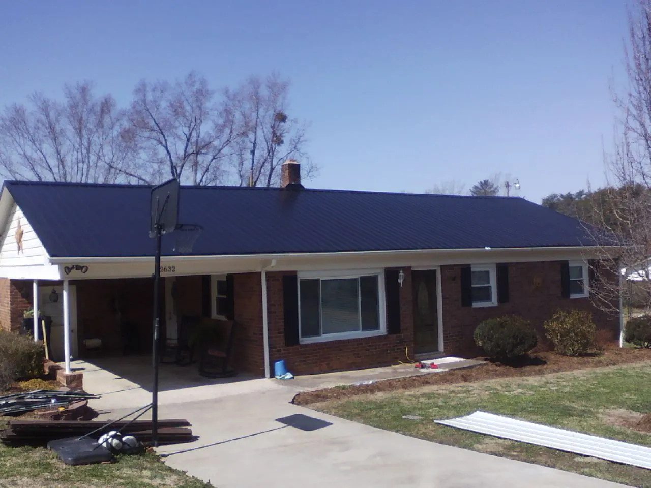 Finished dark blue metal roof on a brick ranch with a carport in Pelahatchie