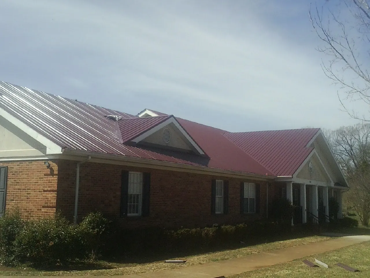 Red metal roof with gabled entries on a long brick building, from a Hail Damage Roof Repair job in Pelahatchie