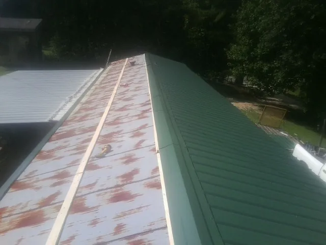 Old rusted panels beside newly installed green metal roofing — Wind Damage Roof Repair by Roofing Brothers in Pelahatchie