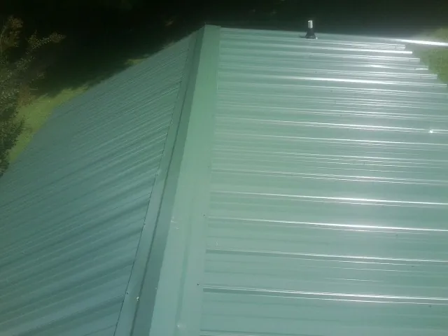 New green metal panels meeting at the ridge of a roof — Flat Roof Repair work by our crew in Pelahatchie