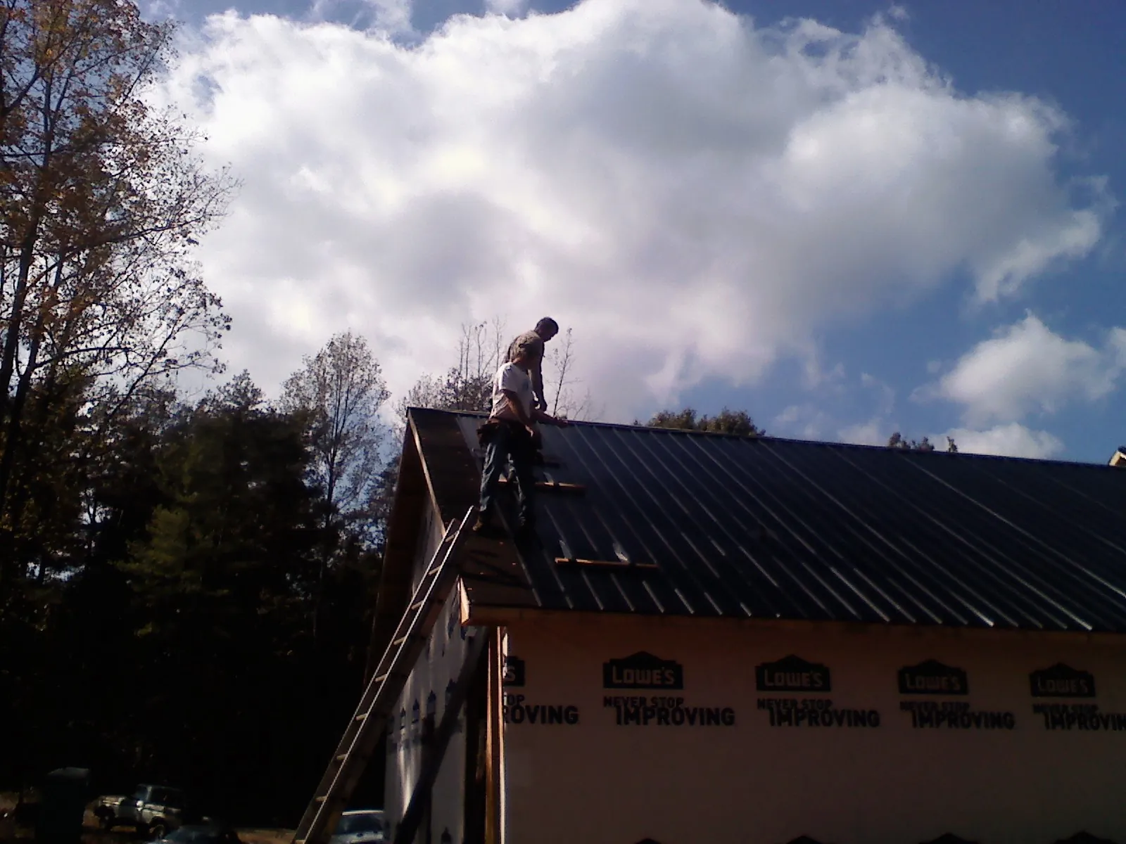 Roofer fastening dark metal panels high against a cloudy sky, from a Roof Inspection job in Pelahatchie