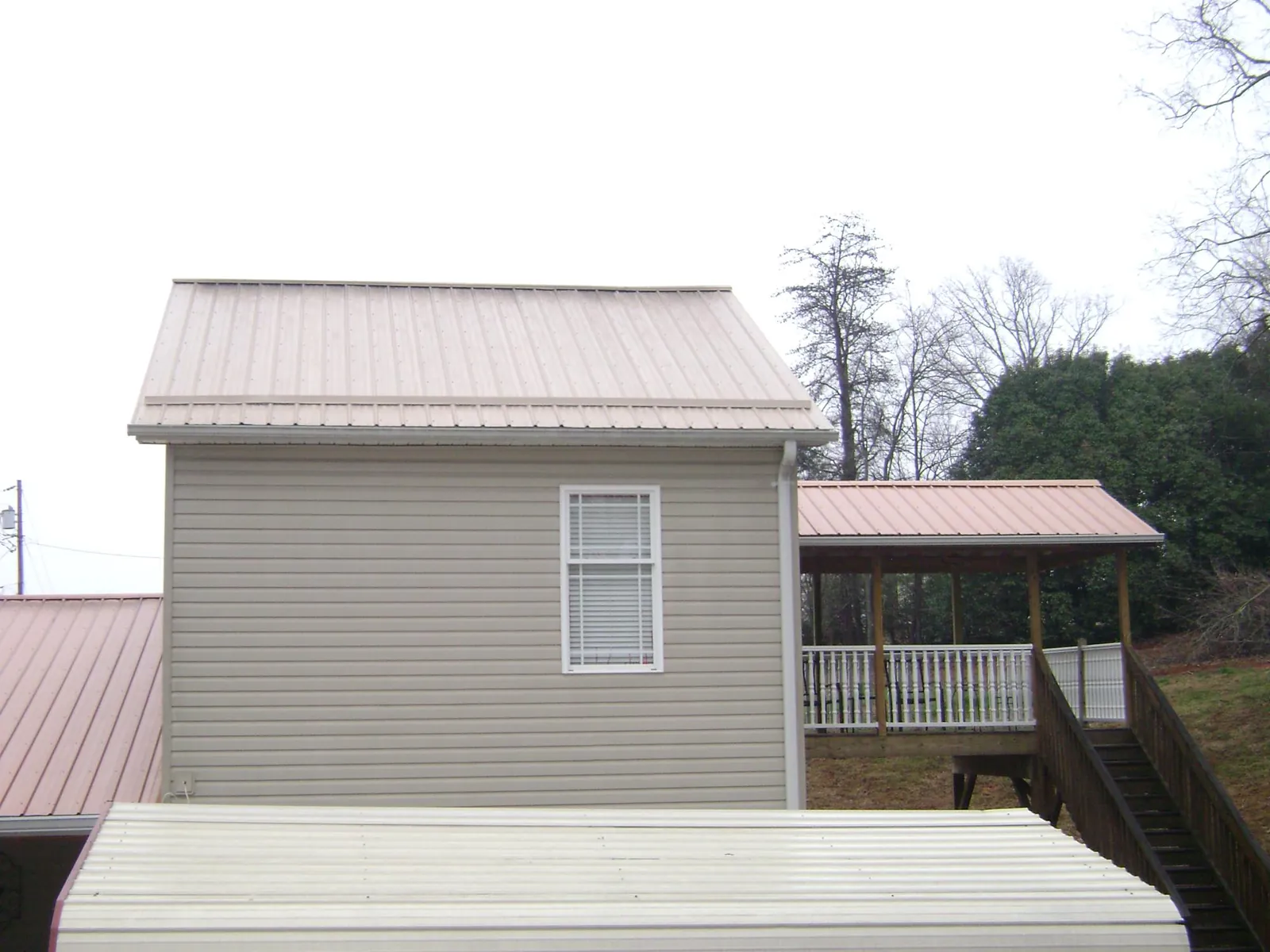 Tan metal roofs on a two story addition and attached porch, from a Roof Replacement job in Pelahatchie